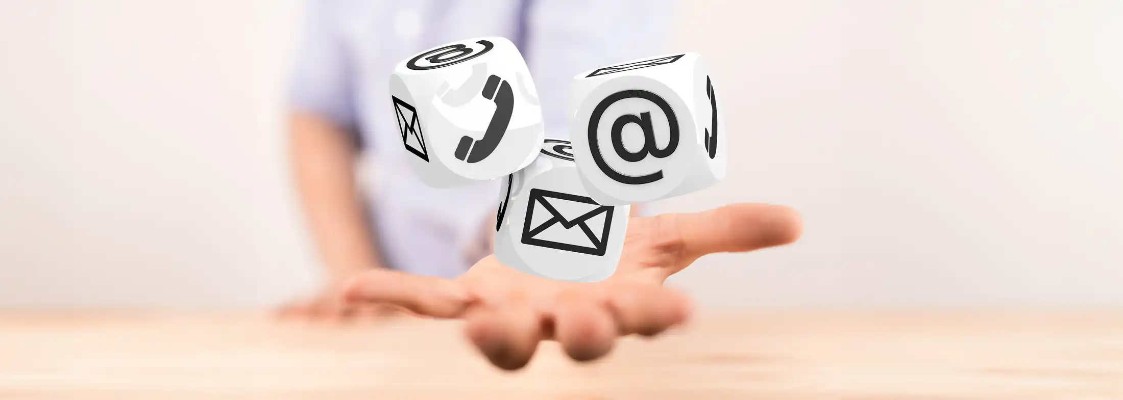 Hand im Vordergrund, die drei Würfel mit Symbolen für E-Mail, Telefon und Post wirft